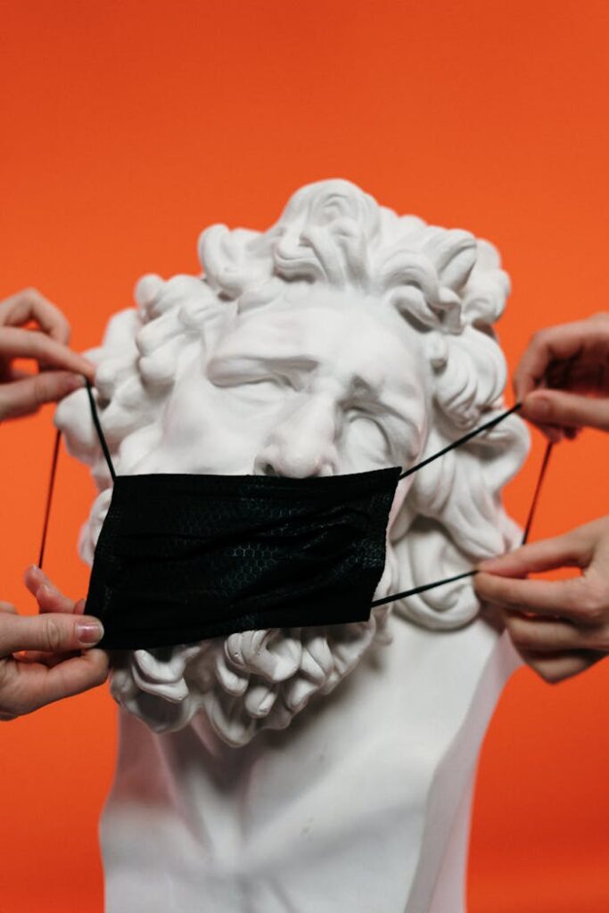 pexels photo 3952229 Classical white statue with black face mask against orange background, symbolizing protection.